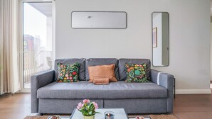 Un salon moderne avec un canapé gris, des coussins colorés, une table basse ornée d’un vase de fleurs et un grand miroir accroché au mur.