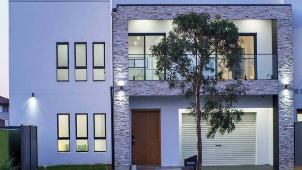 A modern two-story house with a flat roof, large windows, and a brick accent wall.