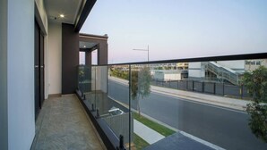 A modern balcony with a glass railing overlooking a street and buildings.