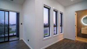 A modern apartment with a large sliding glass door leading to a balcony, three windows with black frames, and a wooden floor.