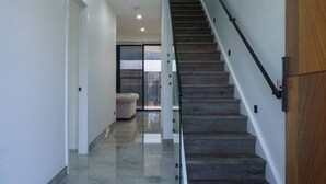 A modern staircase with a wooden finish and glass railings, leading to a room with a large window and a beige sofa.