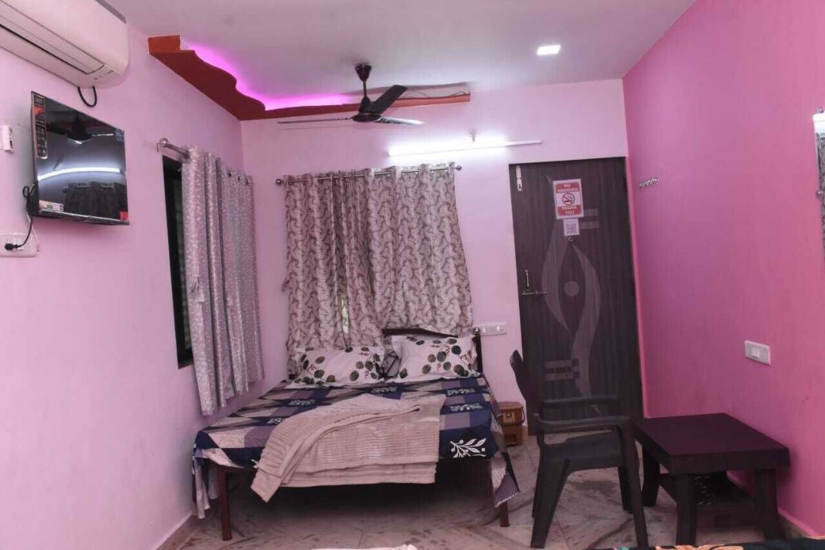 Une chambre à coucher comprenant un lit, une chaise, une petite table, un ventilateur de plafond et un téléviseur.