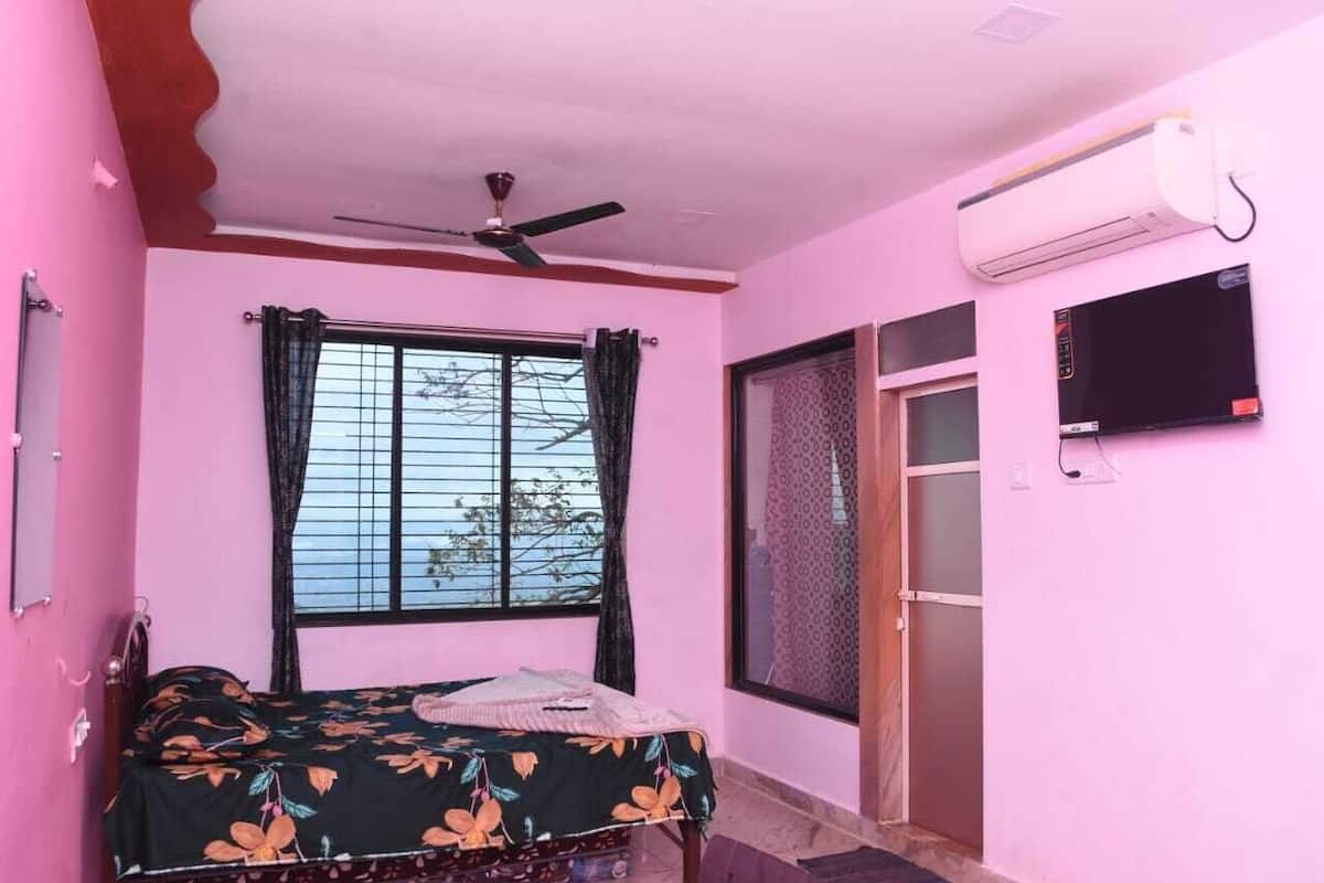 Une chambre avec un lit, un ventilateur de plafond, un climatiseur, une fenêtre avec des rideaux et un téléviseur fixé au mur.