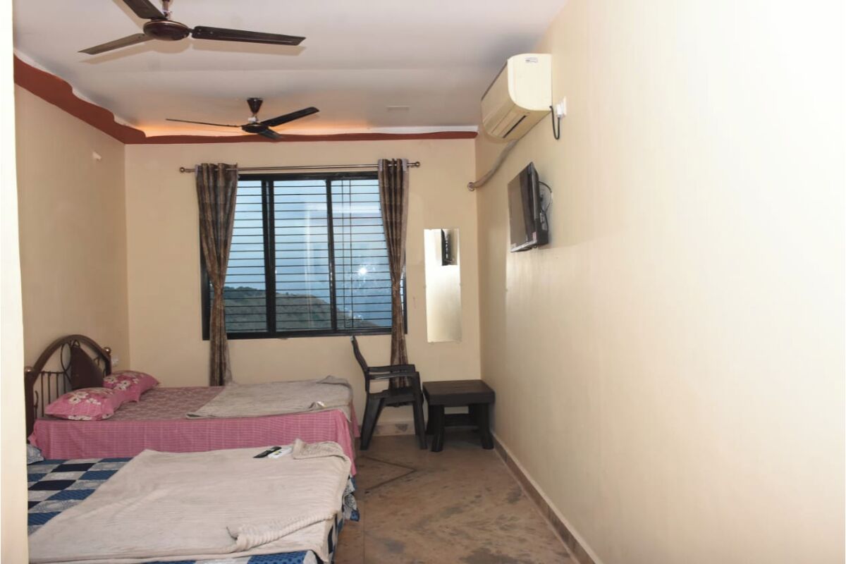 A bedroom with two beds, a ceiling fan, an air conditioner, a window with curtains, and a small table.