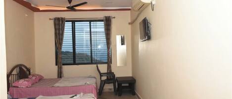 A bedroom with two beds, a ceiling fan, an air conditioner, a window with curtains, and a small table.