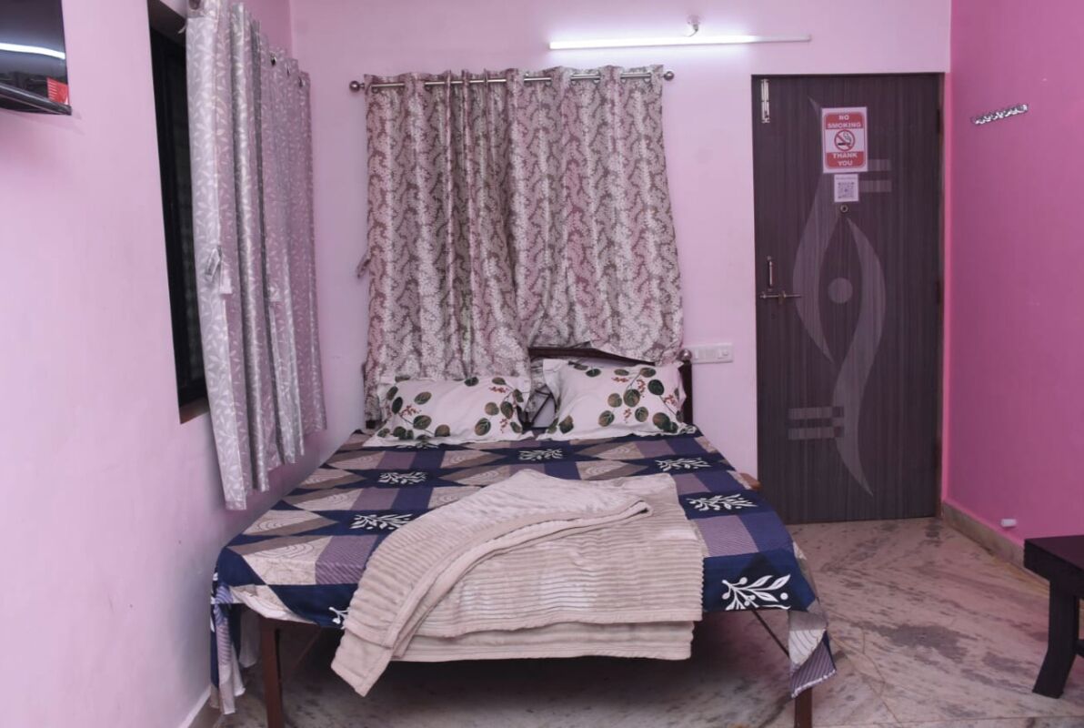 A bedroom with a bed, curtains, a door, and a wall-mounted light fixture.