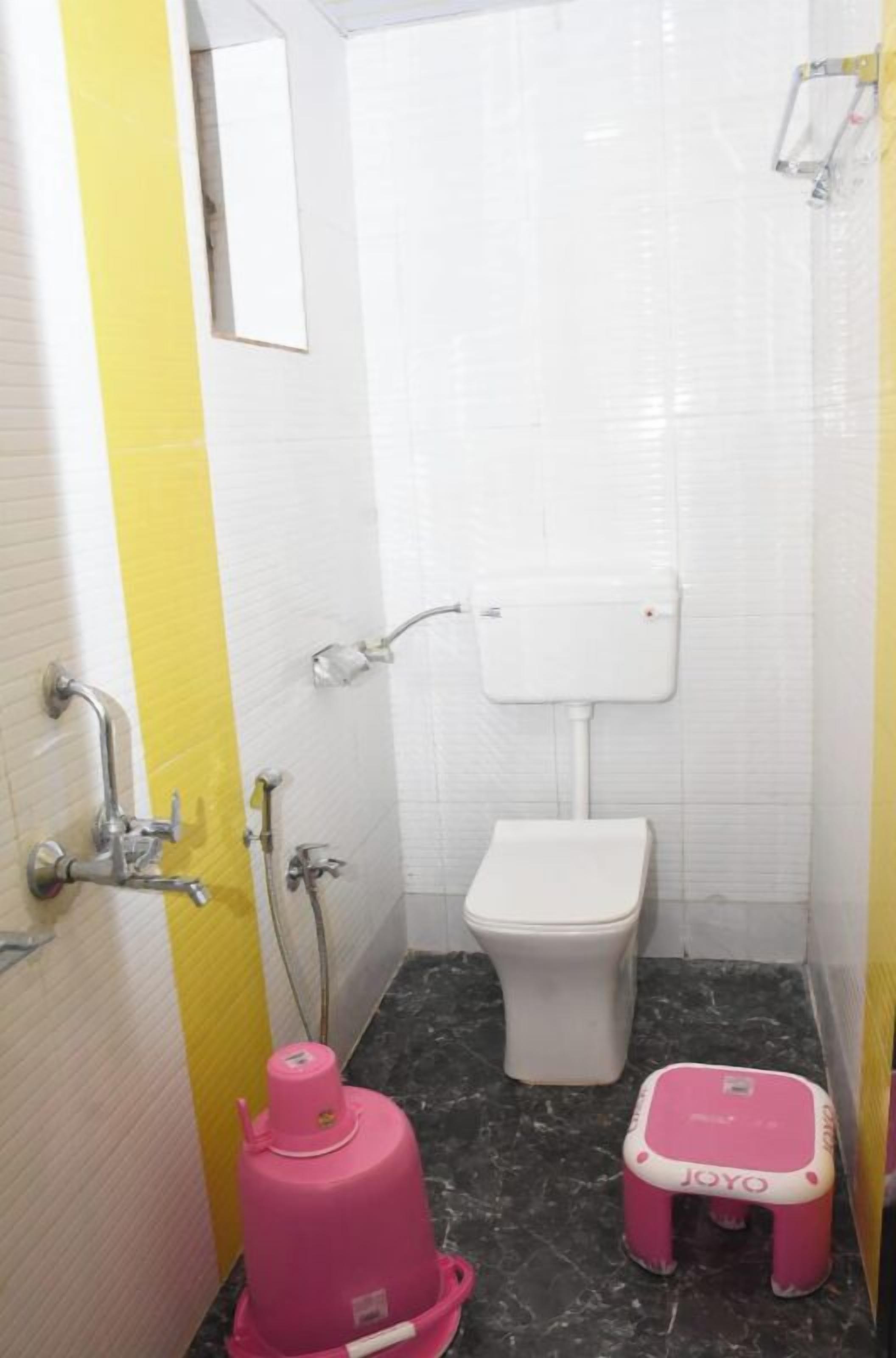 A small bathroom with a white toilet, a pink water heater, and a pink step stool.