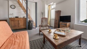 A living room with a sofa, a wooden coffee table with cups and saucers, a television, and a staircase. - Village house for 4 people, 500m from the sea (La Bernerie-en-Retz)