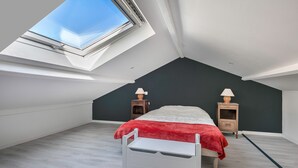 A high-ceilinged bedroom with a skylight, a bed with a red blanket, two bedside tables with lamps, and a white bench. - Village house for 4 people, 500m from the sea (La Bernerie-en-Retz)