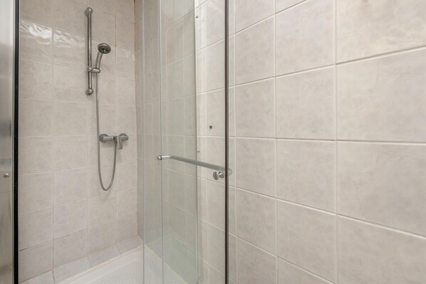 A shower area with a glass door, a handheld showerhead, and a wall-mounted faucet.