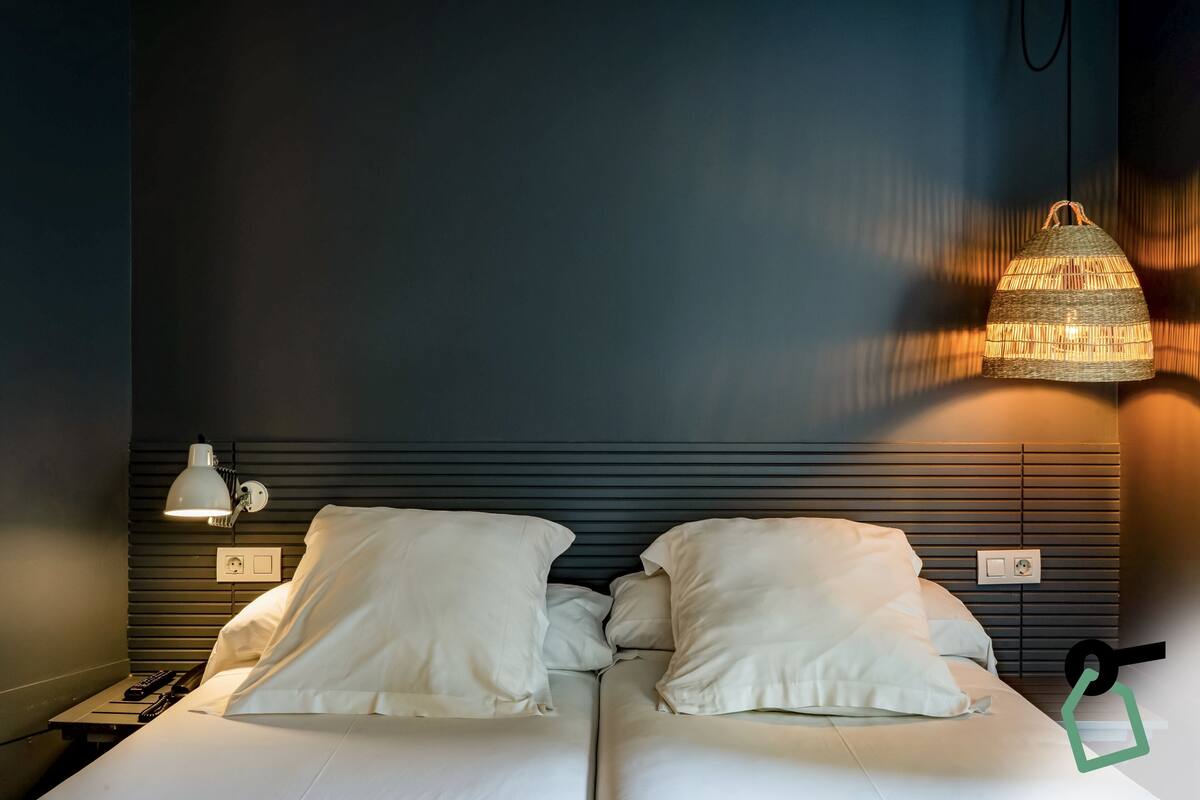 A hotel room with a bed, a bedside lamp, and a hanging light fixture.