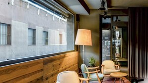 A modern room with wooden paneling, a large window with metal bars, a floor lamp, and a small table with chairs. - Hotiday Barcelona Colom (Barcelona)