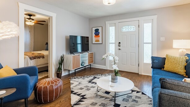 Un salon moderne comprenant un canapé, un pouf, une table basse et un téléviseur posé sur un meuble.