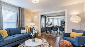 Un salon moderne avec un canapé bleu, une table basse et, au fond, un coin repas.