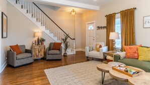 A spacious living room with a staircase, wooden flooring, and a mix of sofas and chairs.