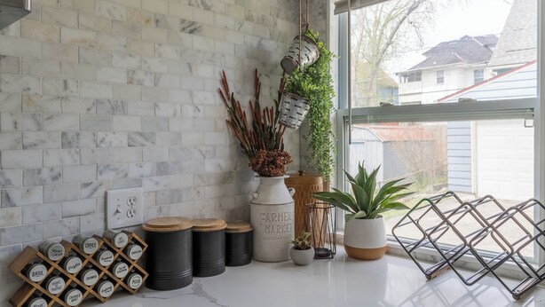 A kitchen with white marble tiles, hanging planters, and a window with a view of a house.