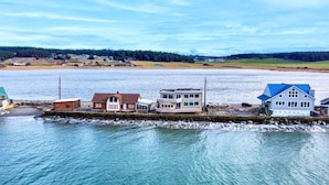 A coastal property with a dock, a house with a blue roof, and a building with multiple windows. - 2 BR Unit w/ Mesmerizing Water View @Oak Harbor (Oak Harbor)