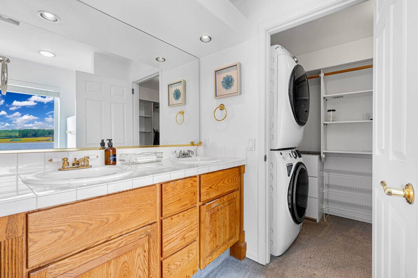 A modern bathroom with a large mirror, two sinks, wooden cabinetry, and a built-in washer and dryer.
