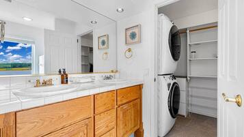 A modern bathroom with a large mirror, two sinks, wooden cabinetry, and a built-in washer and dryer.