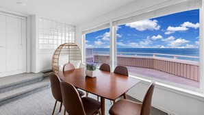 A dining area with a wooden table and chairs, a woven chair, and a view of the ocean through large windows. - 2 BR Unit w/ Mesmerizing Water View @Oak Harbor (Oak Harbor)