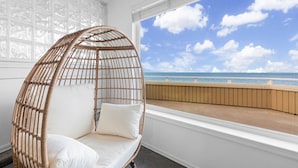 A room with a large window overlooking a beach, a wicker chair with cushions, and a patterned wall. - 2 BR Unit w/ Mesmerizing Water View @Oak Harbor (Oak Harbor)
