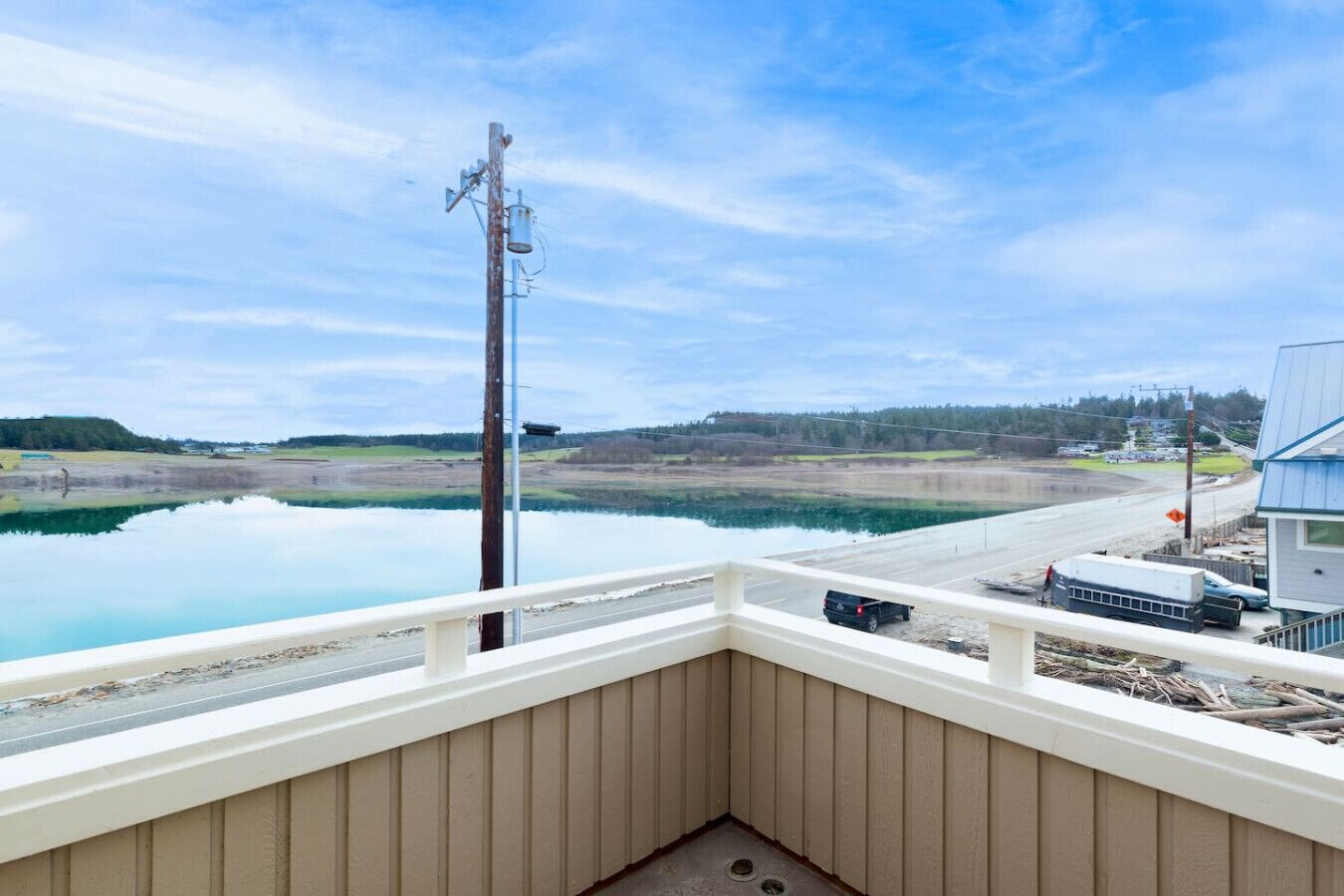 Un balcon donnant sur un lac paisible, un poteau électrique et une rive lointaine.
