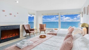 Een hotelkamer met een open haard, twee fauteuils, een bed met uitzicht op de oceaan en een groot raam.