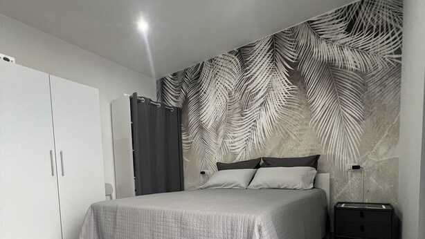 A bedroom with a bed, a wardrobe, a nightstand, and a wall with a leaf pattern. - Your retreat in the heart of Cagliari, sea and fun at your doorstep! (Cagliari)