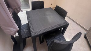 A small, enclosed patio area with a black woven table and chairs, a white wall with a fire extinguisher, and a door leading outside. - Your retreat in the heart of Cagliari, sea and fun at your doorstep! (Cagliari)