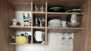 A compact kitchen with a stainless steel sink, a built-in stove, and wooden shelves holding kitchenware and utensils. - Your retreat in the heart of Cagliari, sea and fun at your doorstep! (Cagliari)