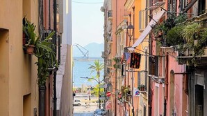 A narrow street lined with colorful buildings, a parked car, and a view of the sea in the distance. - Your retreat in the heart of Cagliari, sea and fun at your doorstep! (Cagliari)