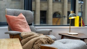 A modern living room with a grey armchair, a pink pillow, a throw blanket, and a small side table with a lamp. - Curated 2B/2B DT Halifax (Halifax)