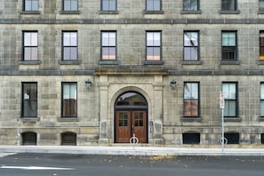 A multi-story stone building with a central arched entrance, multiple windows, and a street in front. - Curated 2B/2B DT Halifax (Halifax)
