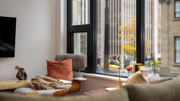 A modern living room with a sofa, a small table, and a window with a view of a cityscape. - Curated 2B/2B DT Halifax (Halifax)