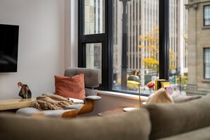 A modern living room with a sofa, a small table, and a window with a view of a cityscape. - Curated 2B/2B DT Halifax (Halifax)