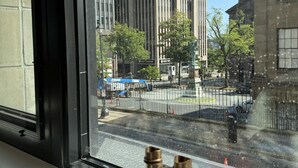 A window with binoculars on the sill, overlooking a street with tall buildings and a clear sky.