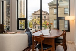 A modern living room with a large window, a round wooden dining table, and a comfortable sofa. - *NEW Designer Mid-Century Modern 2B/2B (Halifax)