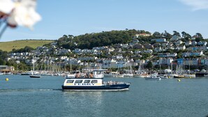Un traversier portant l’inscription « FERRY » sur le côté était amarré dans un port où se trouvaient plusieurs bateaux, avec, en arrière-plan, une colline densément peuplée, parsemée de maisons.