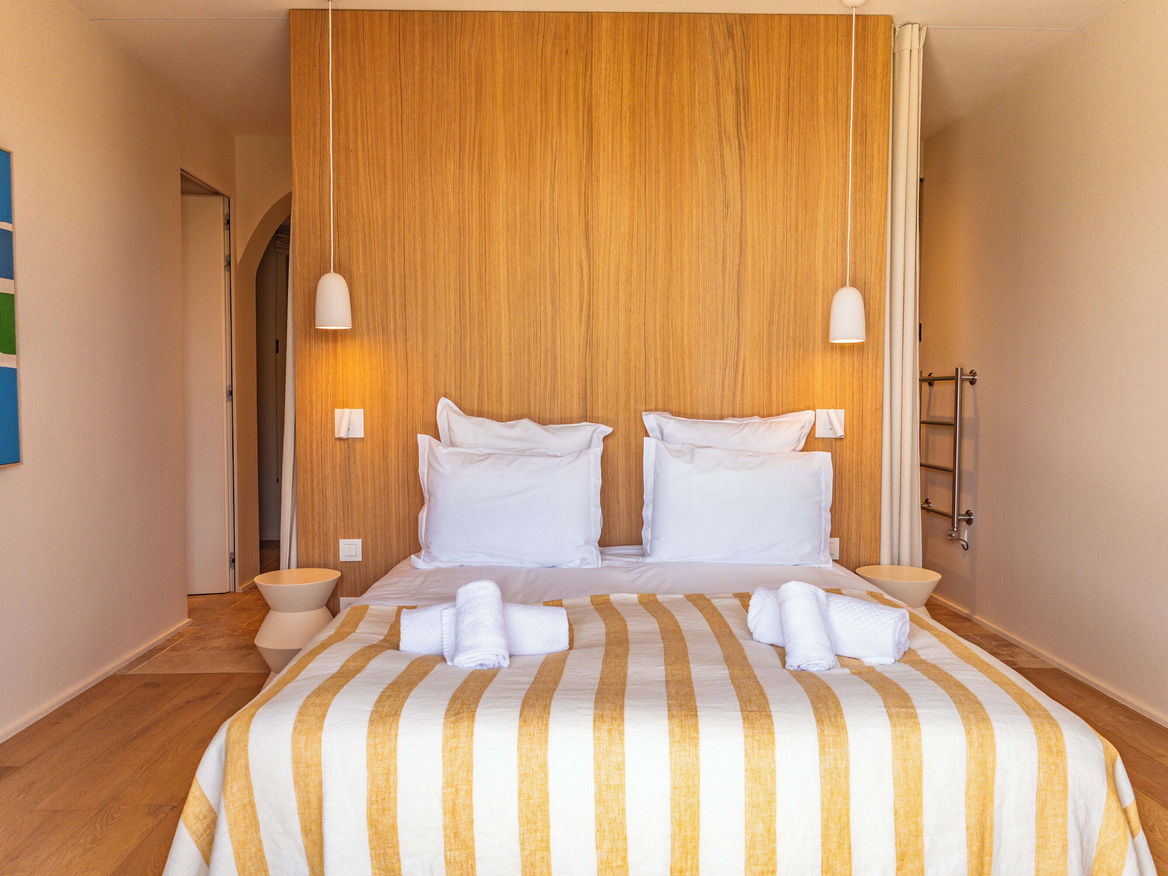 A hotel room with a large bed, two bedside tables, a wooden headboard, and a wooden floor.