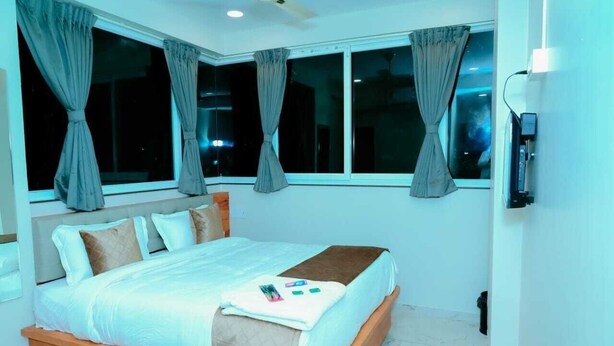 A bedroom with a bed, curtains, a ceiling fan, and a nightstand. - Shivprakash Executive  (Tuljapur)