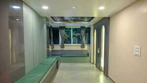A hallway with a green bench, a ceiling fan, and a window with curtains. - Shivprakash Executive  (Tuljapur)