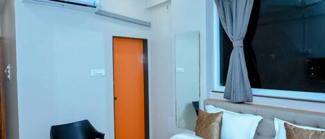 Ein Hotelzimmer mit Bett, Stuhl, Klimaanlage, Fenster mit Vorhängen und einer Tür.