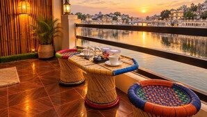 A balcony with a view of a river and buildings, featuring wicker furniture and a table with a cup and saucer. - Venice View Hotel & Restaurant (Udaipur)