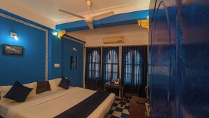 A hotel room with a bed, a desk, a chair, a ceiling fan, and an air conditioning unit. - Venice View Hotel & Restaurant (Udaipur)