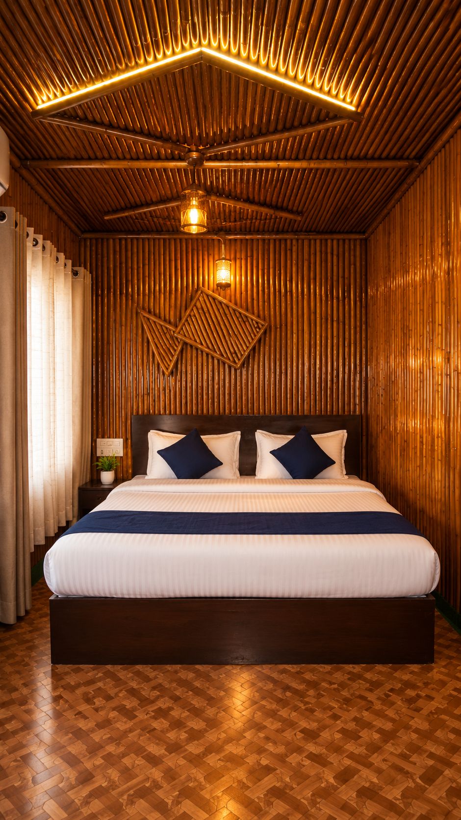A hotel room with a large bed, wooden panel walls, a ceiling fan, and a nightstand with a lamp.