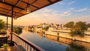A balcony with a view of a river, a cityscape, and a traditional building with a reflection in the water. - Venice View Hotel & Restaurant (Udaipur)