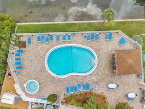 Vista aérea de una zona de piscina con múltiples tumbonas, una piscina central y una piscina circular pequeña.
