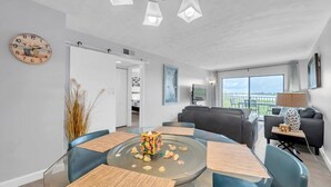Un salón moderno con una mesa de comedor de vidrio, sillas azules, un sofá y un balcón con vistas.