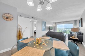 Un soggiorno moderno con tavolo da pranzo in vetro, sedie blu, un divano e un balcone con vista.