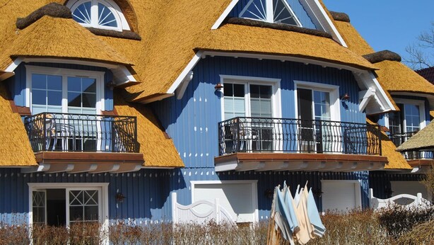 A blue building with a thatched roof, white windows, and balconies with black railings.